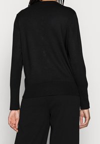 Black knitted sweater with a round neckline, ribbed cuffs, and hem. Smooth texture, fitted design, shown from the back.
