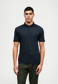 Polo de color azul marino con cuello texturizado, tapeta de tres botones y mangas cortas. La tela parece suave y ajustada.