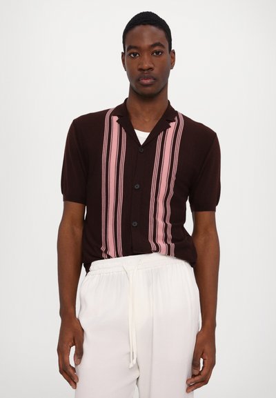 Brown knit shirt with short sleeves, featuring pink vertical stripes and a pointed collar. Black buttons down the front, worn with white pants.