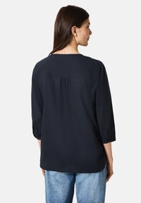 Blusa azul marino con mangas de tres cuartos, textura suave, corte relajado y detalle en la parte trasera con fruncido. Combinada con jeans azul claro.