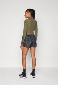 Haut à manches longues ajusté de couleur olive avec une texture côtelée, associé à un short noir avec un motif animal subtil. Chaussures de sport noires aux pieds.