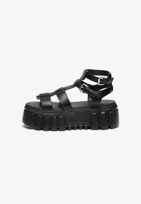 Black platform sandals feature layered straps and buckle accents, with a chunky, textured sole and a smooth footbed design.