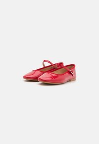Ballerines en cuir verni rouge avec un bout rond, une bride autour de la cheville et un petit détail de boucle métallique. Texture lisse et semelle plate.