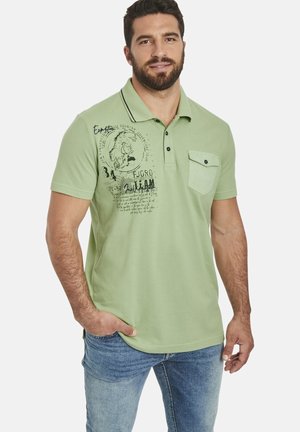 Light green polo shirt made of cotton, featuring a pocket, black buttons, and graphic print with text on one side. Short sleeves and collar.