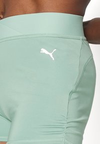 Jasnozielone spodenki sportowe wykonane z gładkiego, elastycznego materiału, z wysokim stanem i małym białym logo Puma po boku.