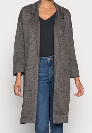 Manteau oversize gris texturé avec de larges revers porté sur un haut noir à col en V et un jean bleu taille haute.
