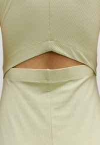 Rippenshirt in hellem Grün mit einem Ausschnitt an der Taille. Der Stoff ist glatt mit einer leicht dehnbaren Textur.
