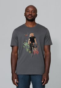 Grijze katoenen t-shirt met een ontwerp van een tijger op een fiets, omringd door kleurrijke bloemen en bladeren. Korte mouwen en ronde hals.