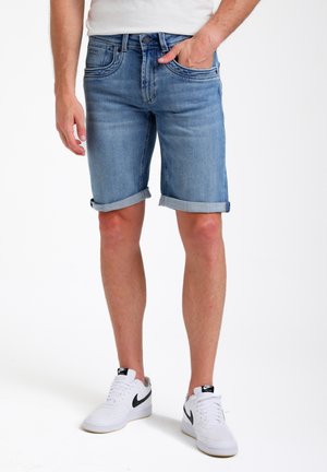 Lichtblauwe denim shorts met een omgerolde zoom, vijf zakken en een subtiele vervaging. Gecombineerd met witte sportieve sneakers.