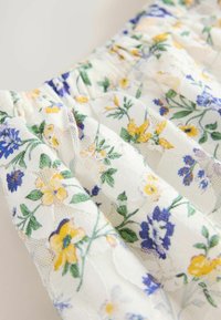 Blumenmusterstoff mit blauen, gelben und weißen Blumen auf einem weißen Hintergrund, mit einem strukturierten, gerafften Design.