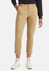 Chinos kaki à coupe droite, avec poignets, deux poches latérales et une fermeture à bouton sur le devant. Tissu en coton doux, détails de couture minimaux.