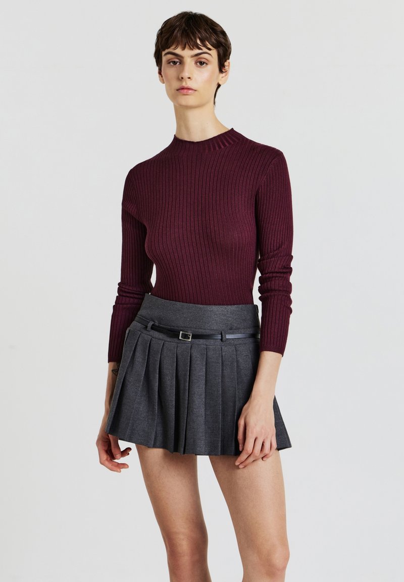 Pull en ribbed bourgogne associé à une jupe plissée grise avec une ceinture à la taille. Le tissu semble lisse et léger.