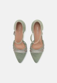 Talons hauts en daim vert avec des bouts pointus, présentant plusieurs lanières ornées de strass et une fermeture à boucle sur le côté.
