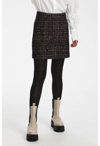 Svart tweed mini kjol med en strukturerad yta, med hög midja. Kombinationen bärs med svarta strumpbyxor och beige ankelboots.