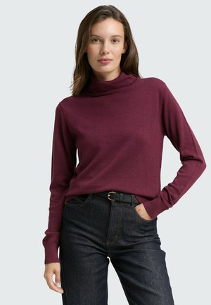 Bordeaux coltrui met ribbelstructuur en lange mouwen, gecombineerd met donkere jeans en een zwarte riem. Eenvoudig, aansluitend ontwerp.