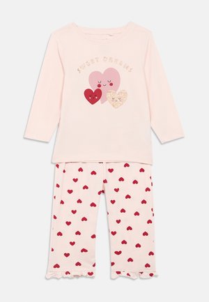 Haut rose clair à manches longues avec trois cœurs souriants et le texte "Sweet Dreams", associé à un pantalon rose recouvert de cœurs rouges et à ourlets volants.