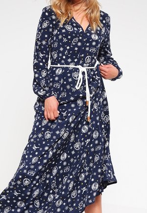 Vestido azul marino con mangas largas, con un patrón cósmico de estrellas y símbolos. Incluye un cinturón blanco y tiene un dobladillo fluido.