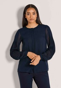 Navyblaue Bluse mit langen, gefalteten, durchsichtigen Ärmeln und einem klassischen Rundhalsausschnitt. Knöpfe vorne und glatte Stofftextur.
