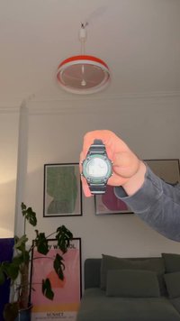 Musta digitaalinen kello pyöreällä kellotaululla, vihreillä yksityiskohdilla, teksturoidulla hihnalla ja valotoiminnolla. Näytössä aika ja digitaalinen asettelu.