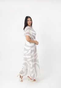 Robe longue et fluide en tissu blanc transparent avec des motifs abstraits gris. Présente des manches courtes et une taille smockée, complétée par des talons légers.