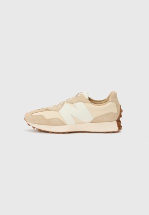 Beżowo-kremowy niski sneaker z białym logo "N", sznurowanym zapięciem i teksturowaną brązową gumową podeszwą skierowany na lewo na białym tle.