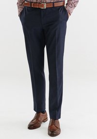 Granatowe spodnie wizytowe o dopasowanym kroju, z delikatnym wzorem w kratkę, gładką strukturą, w połączeniu z brązowymi skórzanymi butami i paskiem.