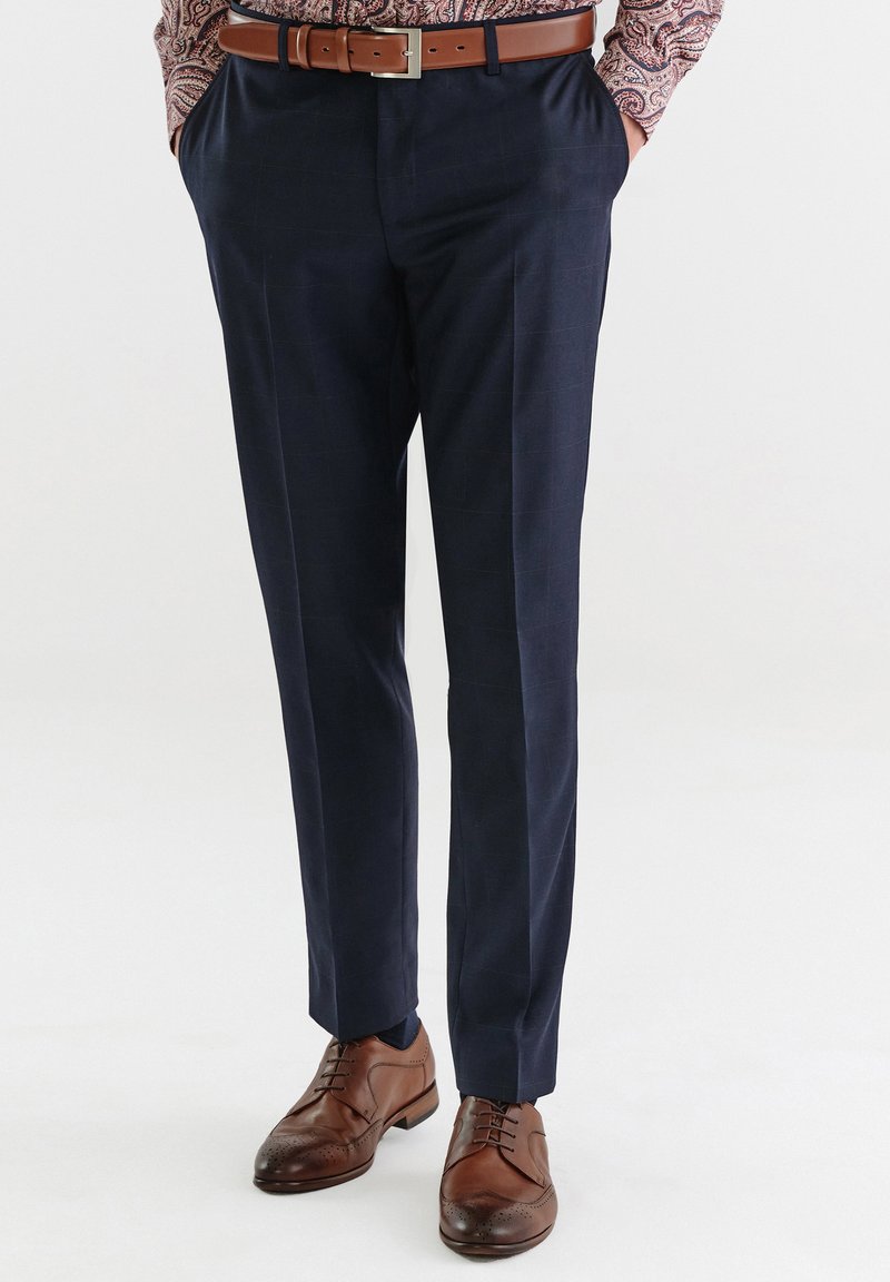 Granatowe spodnie wizytowe o dopasowanym kroju, z delikatnym wzorem w kratkę, gładką strukturą, w połączeniu z brązowymi skórzanymi butami i paskiem.