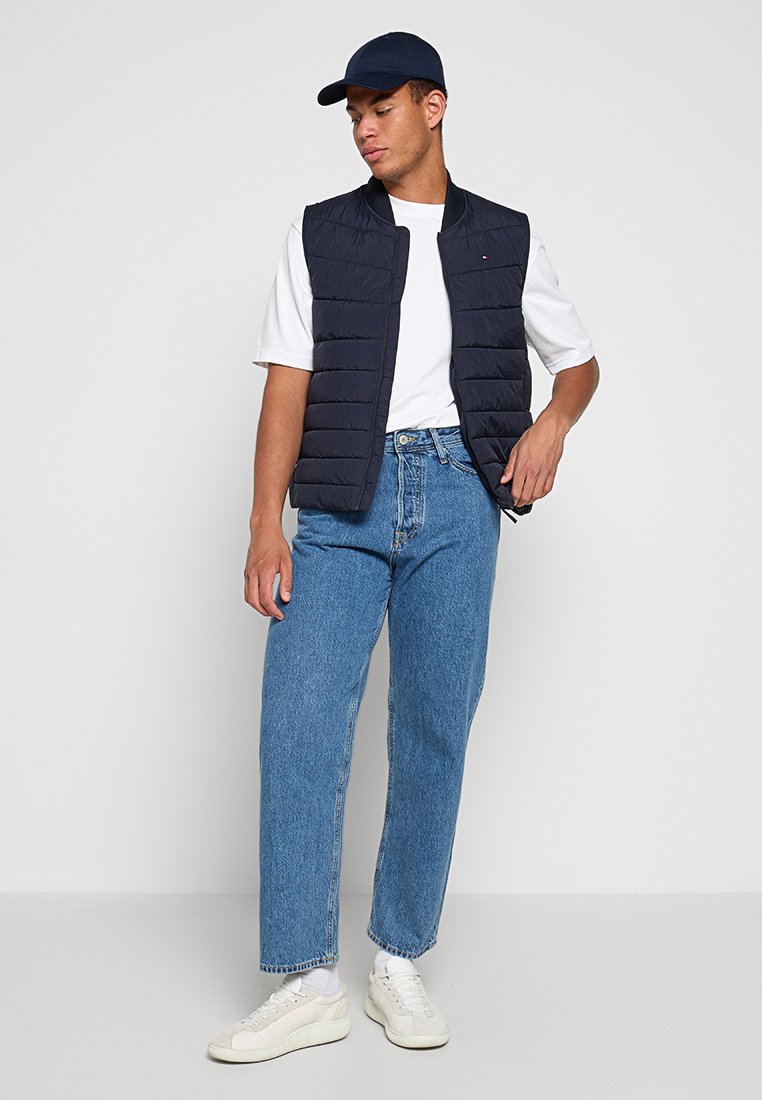 Chaleco acolchado navy, camiseta blanca, jeans rectos de un azul claro y zapatillas blancas. El chaleco cuenta con costuras verticales y un diseño deportivo.