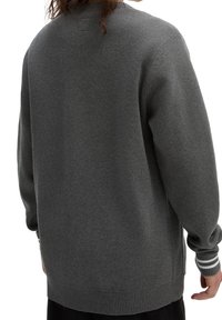 Grå oversized tröja med ribbade ärmslut och fåll, som har ett texturerat tyg och subtila accentstygn längs kanterna.