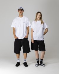 Hvide bomulds t-shirts bæres med sorte denim shorts. Shortsene har kontrasterende syninger. Begge bærer sorte sokker og sko; den ene har en kasket.