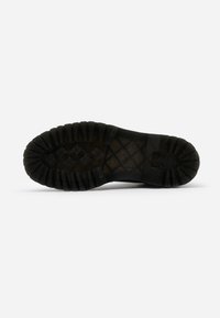 Semelle de bottes noire avec un motif de bande de roulement profond et robuste conçu pour la traction, vue de dessous sur un fond blanc uni.