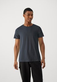 Tricou scurt cu mânecă scurtă, de culoare albastru închis, confecționat din bumbac moale, cu un guler rotund și un croi lejer, asortat cu blugi negri.