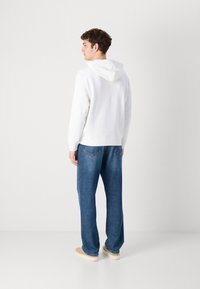 Hanorac alb cu șnur, combinat cu blugi din denim albastru, în croială lejeră. Blugii au buzunare spate cu cusături în contrast.