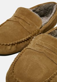 Brune ruskinds loafers med flad sål, der har et syet design og blød, fuzzy foring indvendigt for komfort.