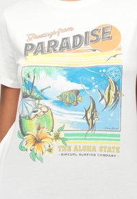 Fehér pamut póló, amely egy színes retró grafikát ábrázol trópusi halakról, kókuszdió italról és virágokról, a "Üdvözlet a PARADICSOMBÓL" felirattal.