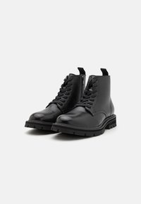 Paire de bottines noires en cuir à lacets avec fermetures éclair latérales et semelles épaisses en caoutchouc sur fond blanc.