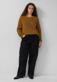 Roestkleurige gebreide trui met een geribbelde textuur, ronde halslijn en lange mouwen, gecombineerd met hooggeplaatste zwarte wijde broek.