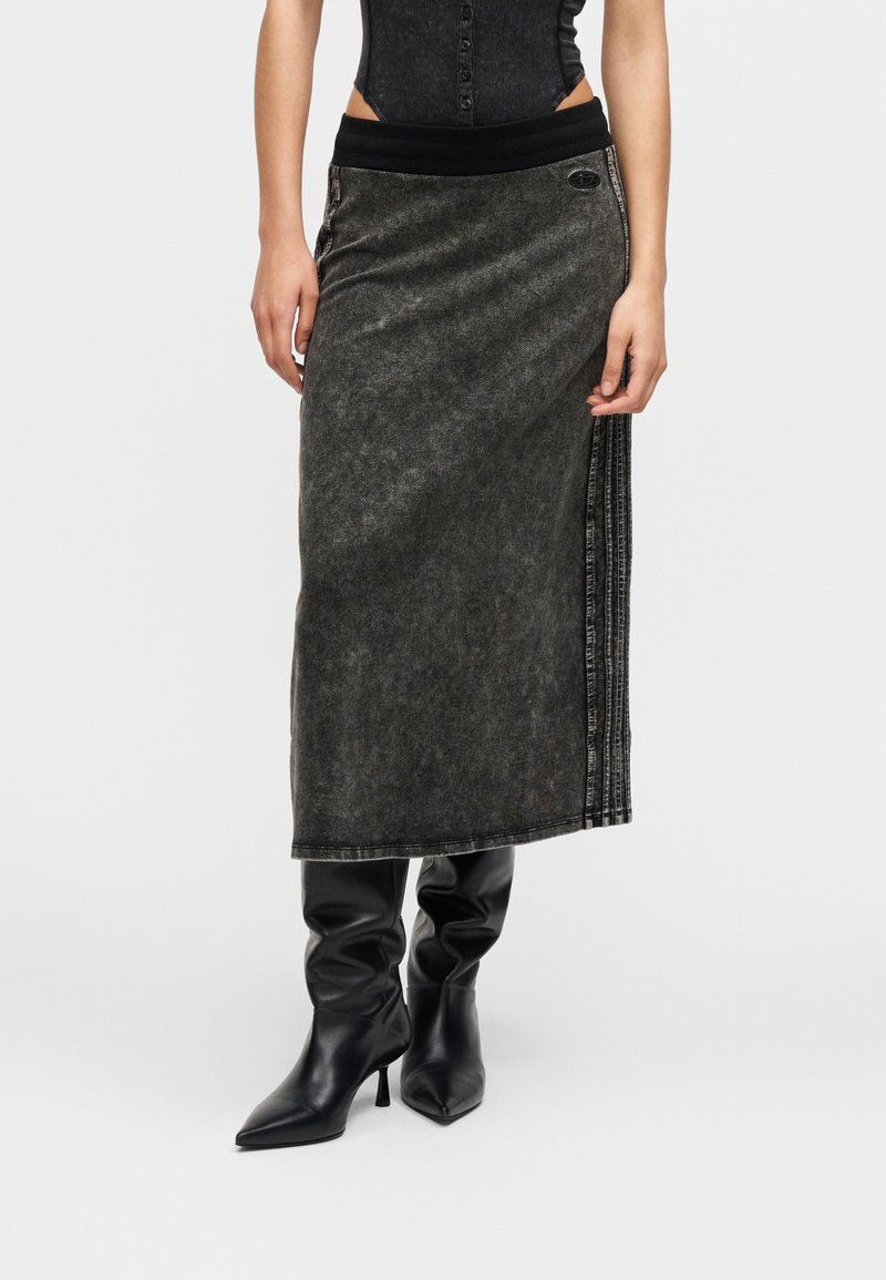 Γυναίκα με μαύρο αμάνικο τοπ, γκρι μίντι φούστα με πλευρικές ρίγες και μαύρα μπότες με τακούνι και μυτερό μύτη, σε λευκό φόντο.