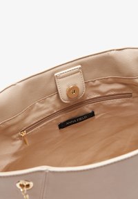 Beige faux leather handbag interior with a satin lining, featuring a zip pocket and a brand label. Smooth texture and gold-tone hardware.