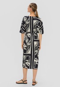 Robe à motifs noirs et crème avec des manches courtes, taille cintrée, longueur mi-mollet et tissu doux. Elle présente des motifs botaniques dans des cadres géométriques.