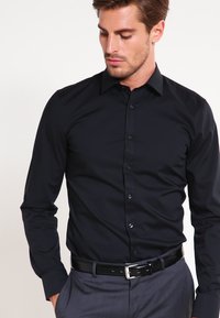 Zwarte blouse met lange mouwen en knoopsluiting aan de voorkant, gemaakt van een gladde stof, voorzien van een kraag en een subtiele glans.