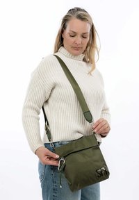 Olive green crossbody bag made of textured fabric, featuring a front zipper pocket and adjustable strap with hardware accents.