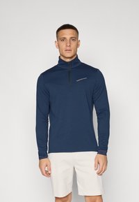 Langarmige, marineblauwe quarter-zip shirt met een soepele textuur en een logo op de borst. Heeft nauwsluitende mouwen en een hoge kraag.