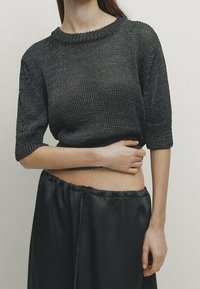 Pull en maille sombre avec un col rond et des manches courtes, assorti à une jupe taille haute en satin noir, mettant en valeur un tissu texturé.