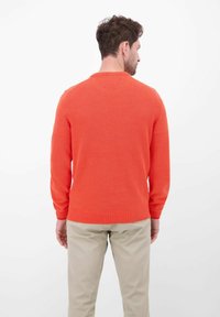 Oranje gebreide trui met een gestructureerd patroon, ronde hals en lange mouwen, gecombineerd met beige taps toelopende broek.