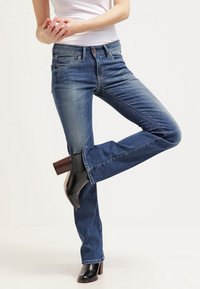 Blå denimjeans med rak passform, som har fem fickor, metallnitar och en blekt tvätt, tillsammans med svarta klackstövlar.