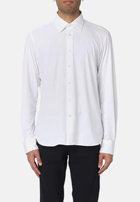 Camicia bianca a maniche lunghe con colletto classico, texture liscia e patta con bottoni frontale, abbinata a pantaloni neri.