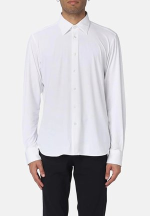 Camicia bianca a maniche lunghe con colletto classico, texture liscia e patta con bottoni frontale, abbinata a pantaloni neri.
