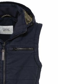 Veste matelassée sans manches bleu marine avec fermeture éclair frontale, poche poitrine zippée, et capuche avec cordon de serrage ajustable.