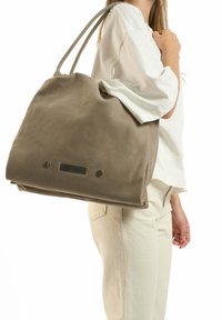 Grote, zachte grijze boodschappentas met twee schouderbanden, voorzien van een gladde textuur en metallic accenten aan de voorkant voor sluiting.